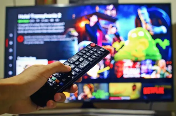 Dłoń trzymająca pilot do telewizora, na ekranie menu platformy streamingowej. Wady i zalety reklamy telewizyjnej – czy warto ją oglądać?